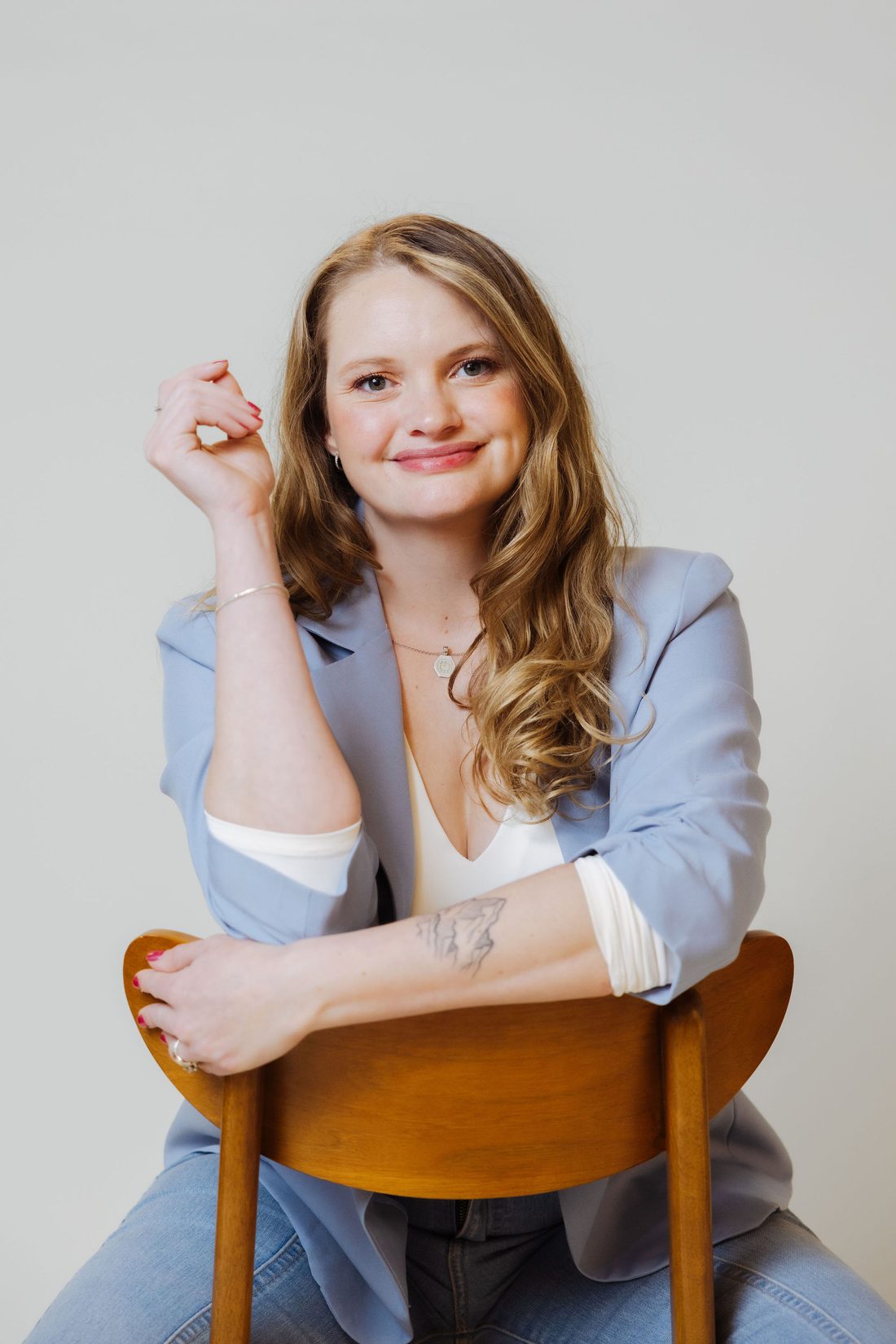 Lauren Bennett seated in a wooden chair, smiling, wearing a light blue blazer